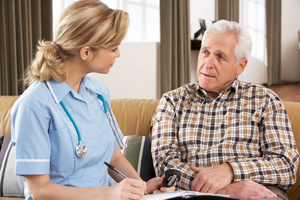 Picture of a female Nurse holding a pen and notepad while looking at an eldery male patient.