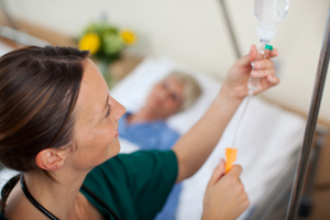 Picture of a female nurse hooking uo sn IV and an elderly female patient lying down in bed,