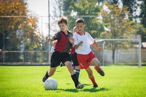 Picture of two young boys outside playing in a soccer game on two different teams.