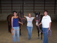 Picture of three females standing next to two horses.