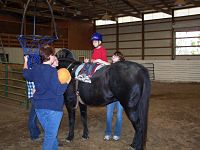 Picture of two females and a child that is wearing a helmet and sitting on top of a horse.